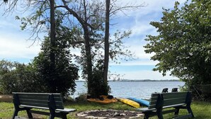 Two benches facing a body of water with kayaks and a stone fire pit in the foreground. - New! A Waterfront Retreat on 14 Acres with 7 Bedrooms That Sleeps 13! (Stella)