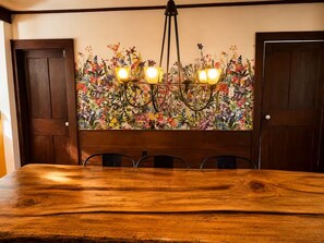 Un comedor con una mesa de madera, cuatro sillas, una lámpara de araña y un mural floral.
