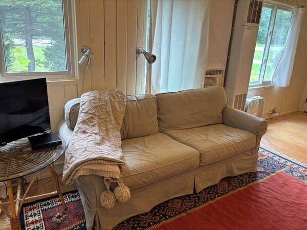 A beige sofa with a knitted throw blanket, a television on a stand, and a patterned rug.