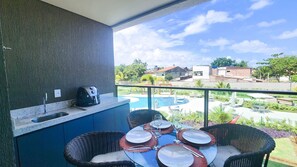 Un balcon doté d’un coin cuisine, d’une table à manger pour quatre personnes et offrant une vue sur une piscine et des immeubles.