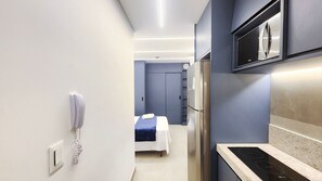 Une chambre d’hôtel moderne équipée d’un lit, d’un minibar, d’un four à micro-ondes intégré et d’un téléphone.