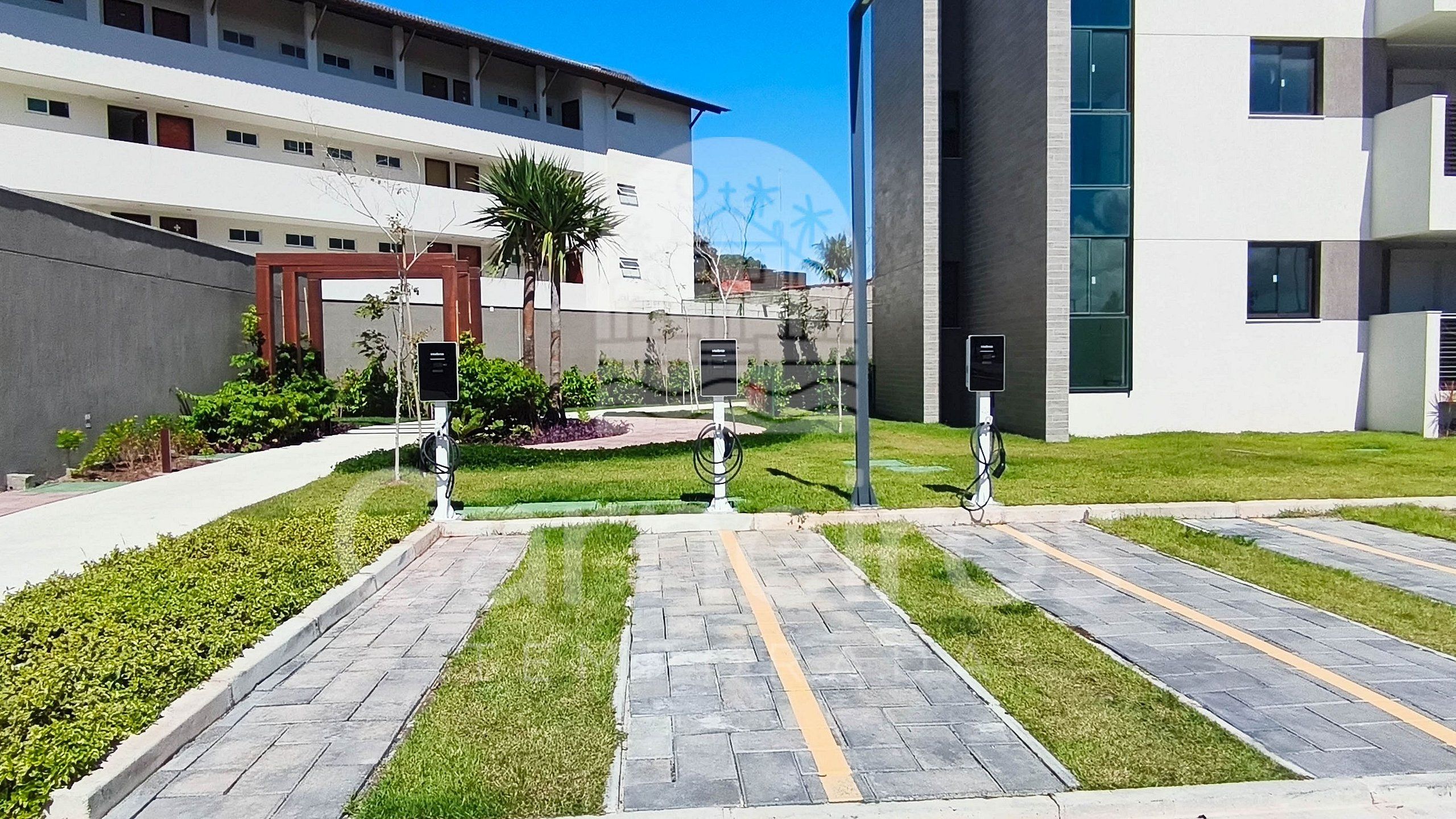 Un bâtiment moderne doté d’une cour dallée, de bornes de recharge électriques extérieures et d’un petit espace jardin.