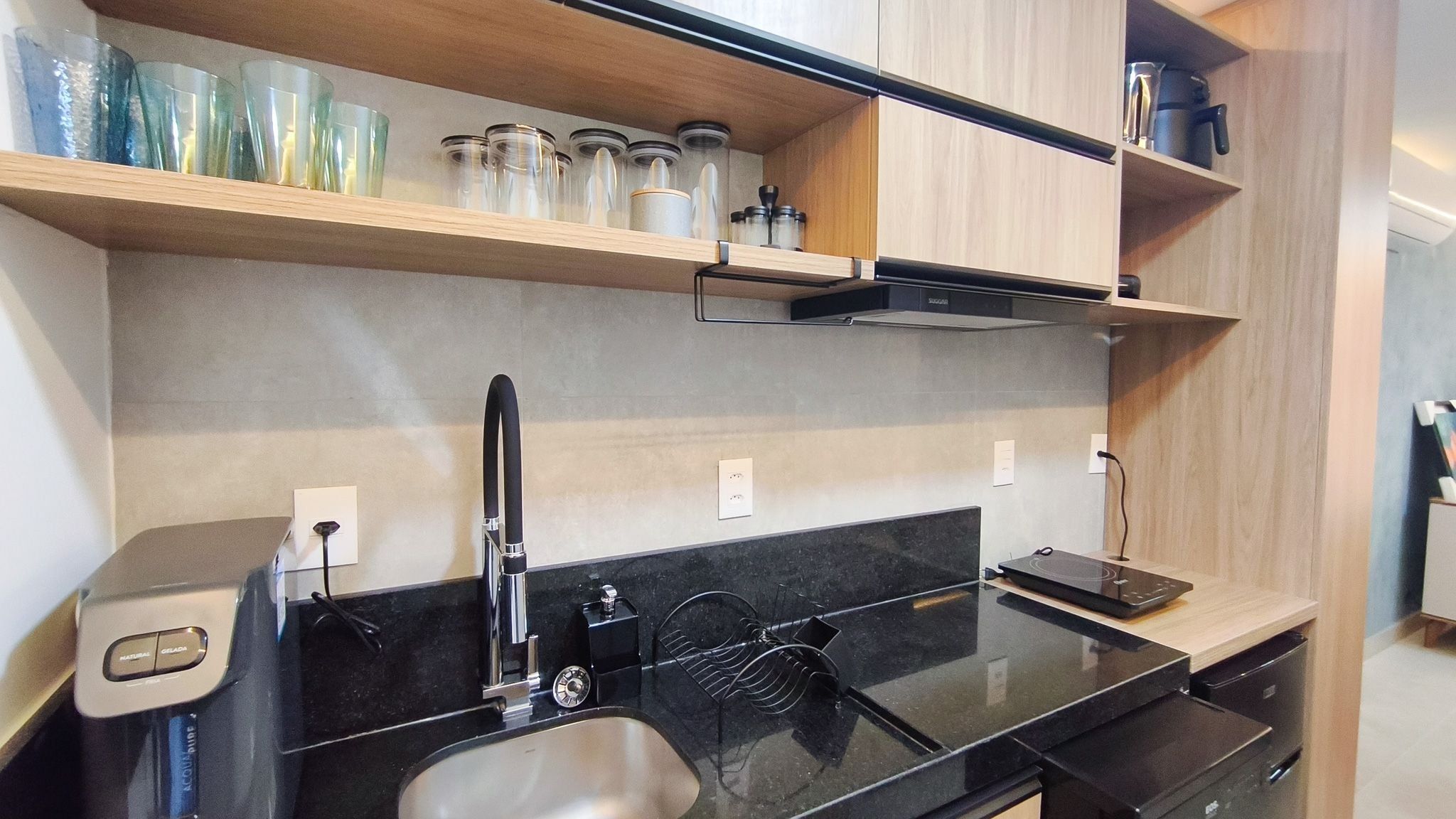 A modern kitchen with a black countertop, stainless steel sink, and wooden shelves above.