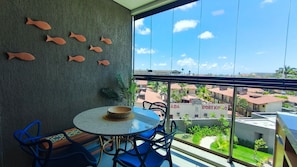 A balcony with a round table, blue chairs, a decorative wall with fish shapes, and a view of buildings and greenery. - Beach Class Summer Residence  (Ipojuca)