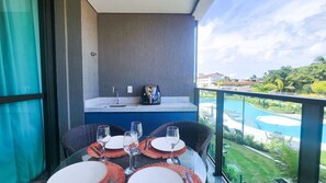 A balcony with a dining table set for four, a coffee maker, and a view of a swimming pool. - Beach Class Summer Residence (Ipojuca)