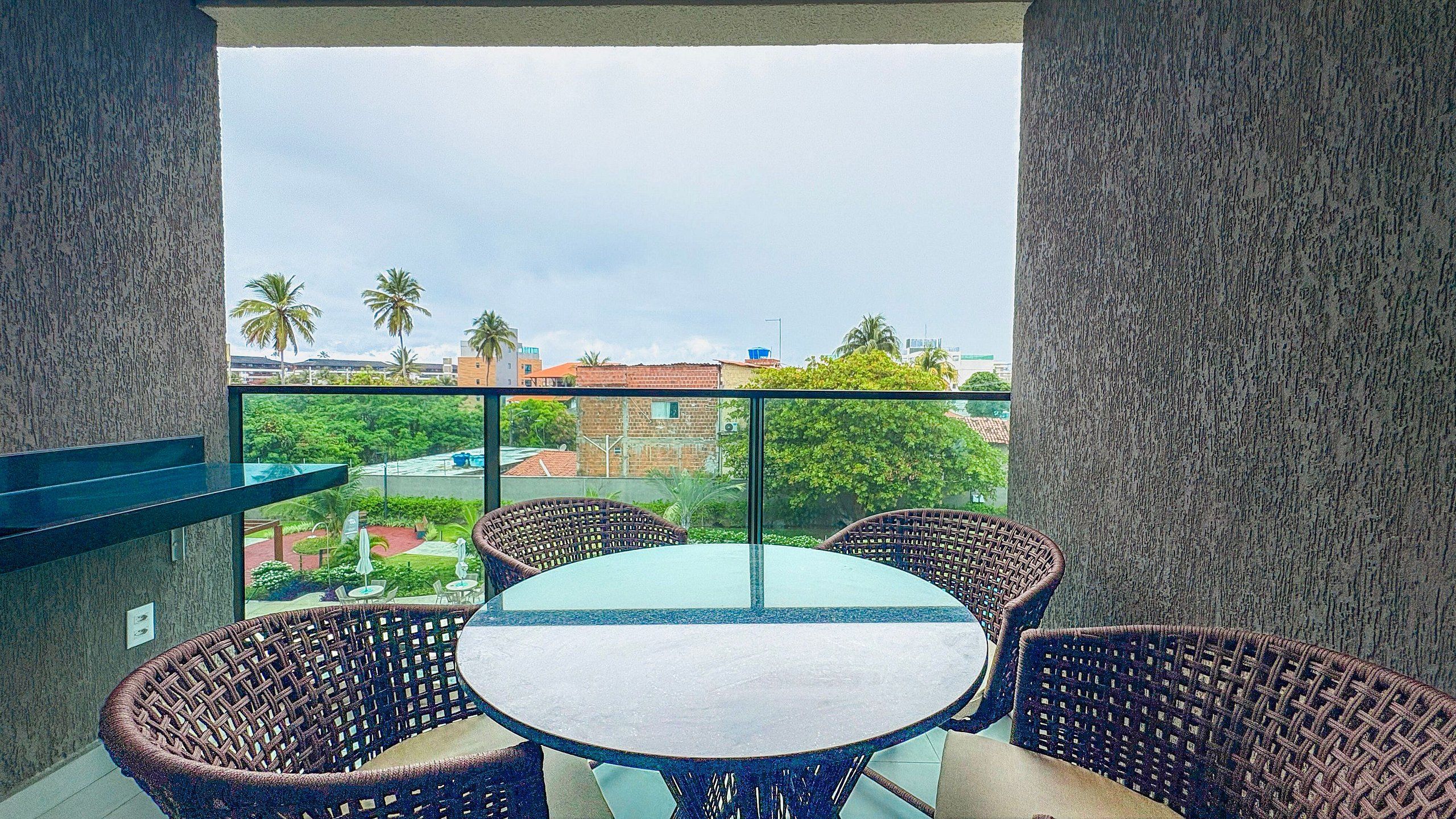 Ein Balkon mit Korbmöbeln und einem Glastisch, mit Blick auf eine Skyline mit Gebäuden und Palmen.