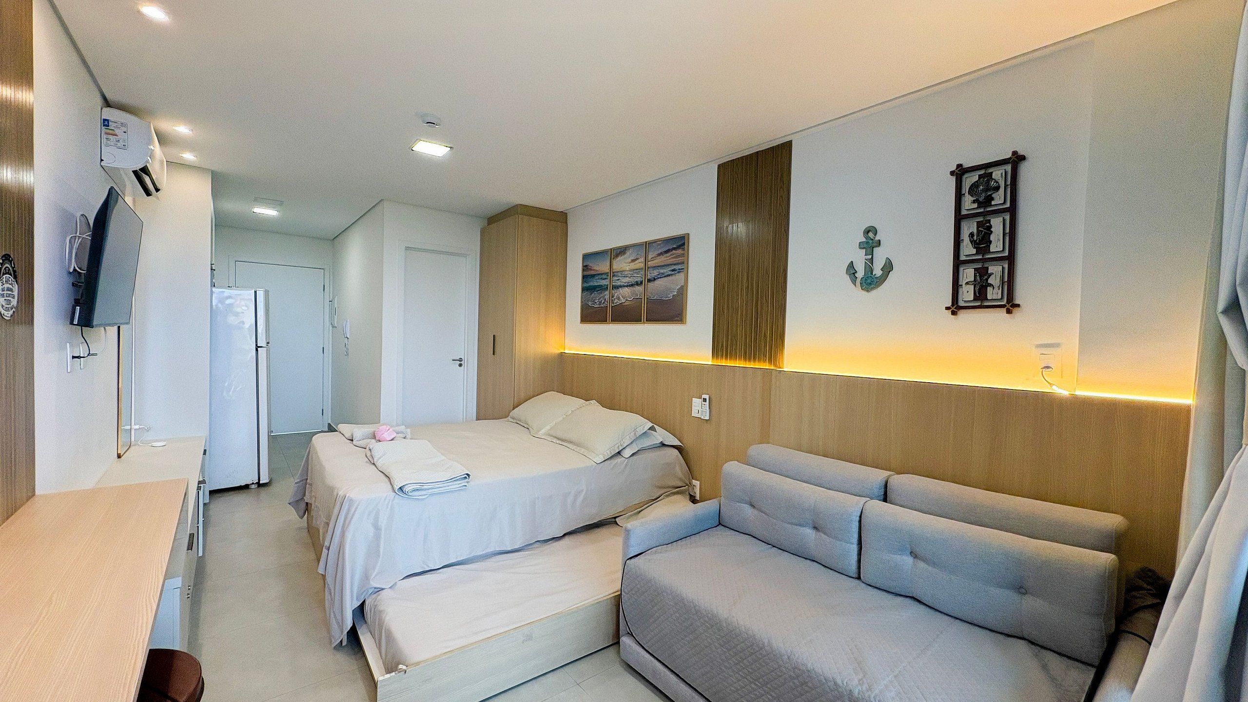 A hotel room with two beds, a sofa, a TV, and a small desk.