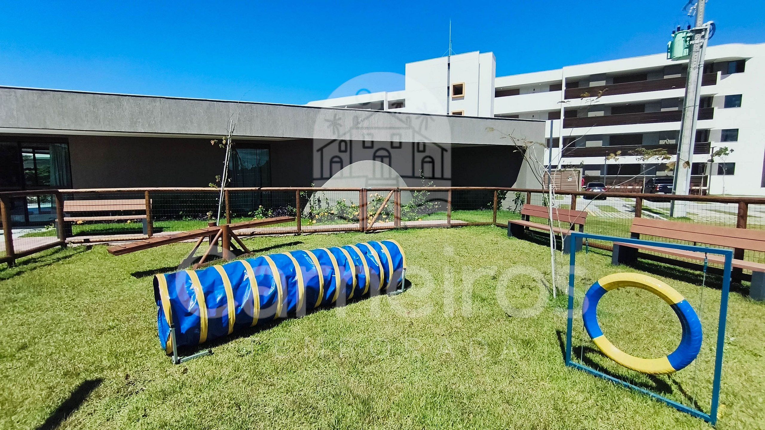 A playground with a blue and yellow tunnel, a yellow and blue ring, and benches.