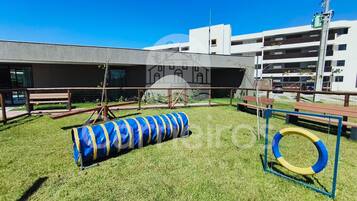A playground with a blue and yellow tunnel, a yellow and blue ring, and benches.