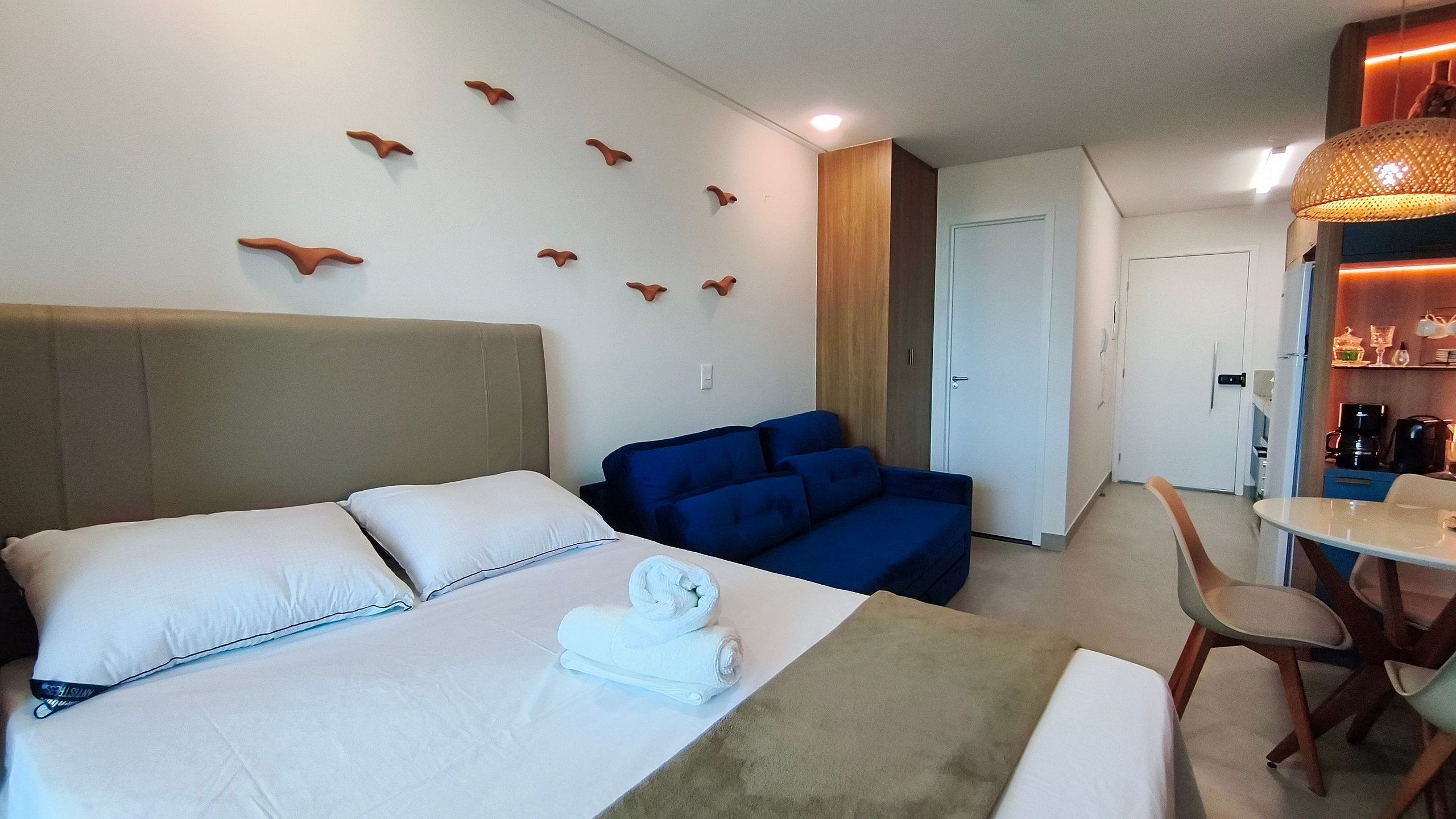 Ett hotellrum med en säng, en blå soffa, ett matbord med stolar och en liten köksdel.