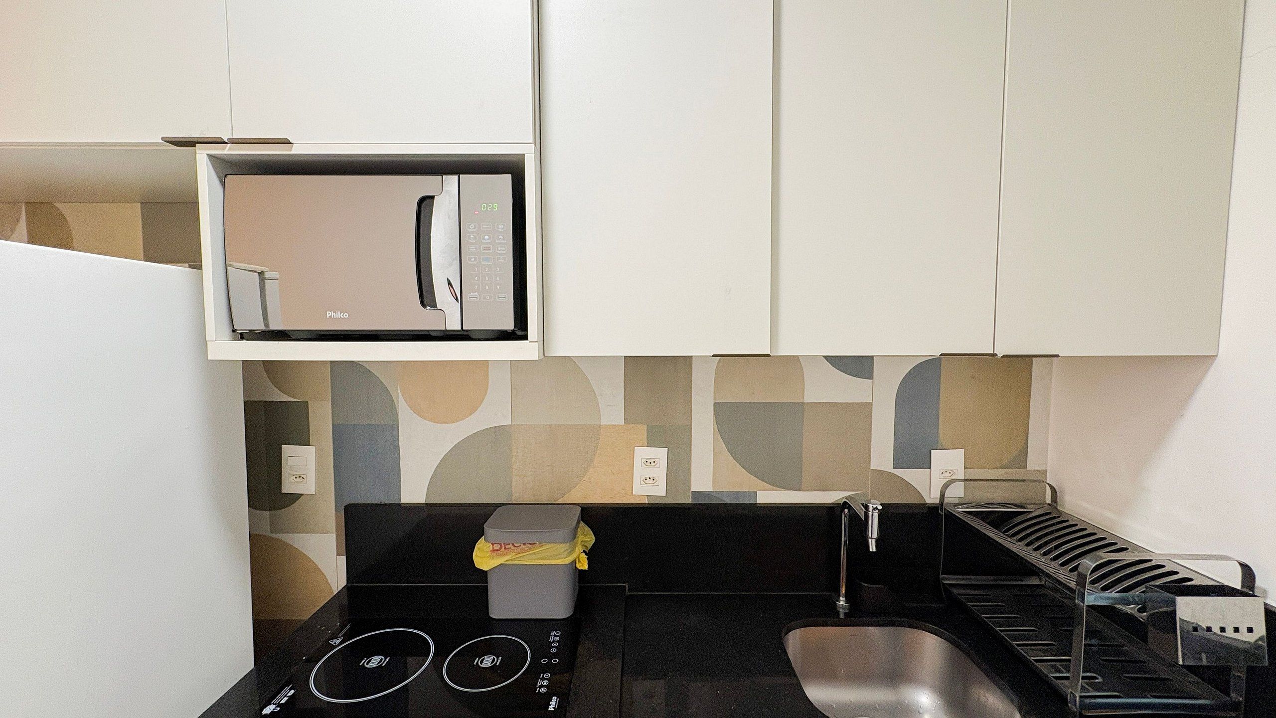 Uma cozinha compacta com micro-ondas, pia e bancada pequena.