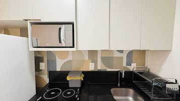 Uma cozinha compacta com micro-ondas, pia e bancada pequena.