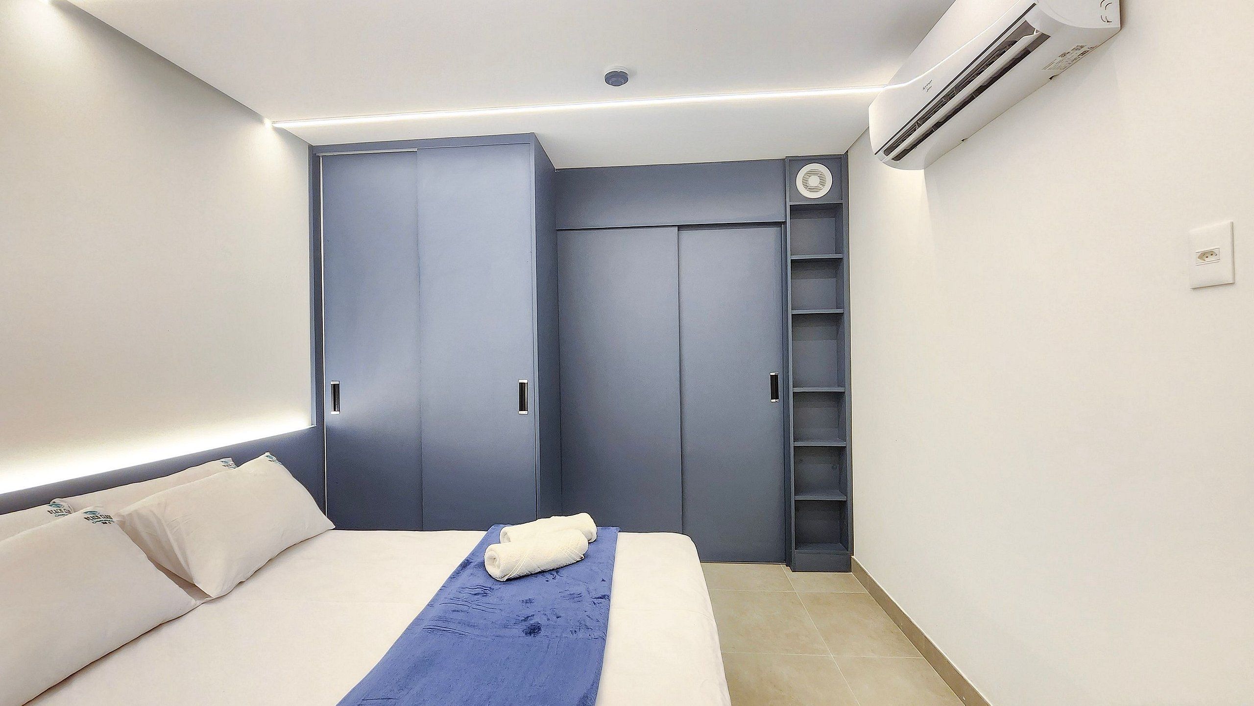A bedroom with a bed, a blue towel, a wardrobe, and an air conditioning unit.