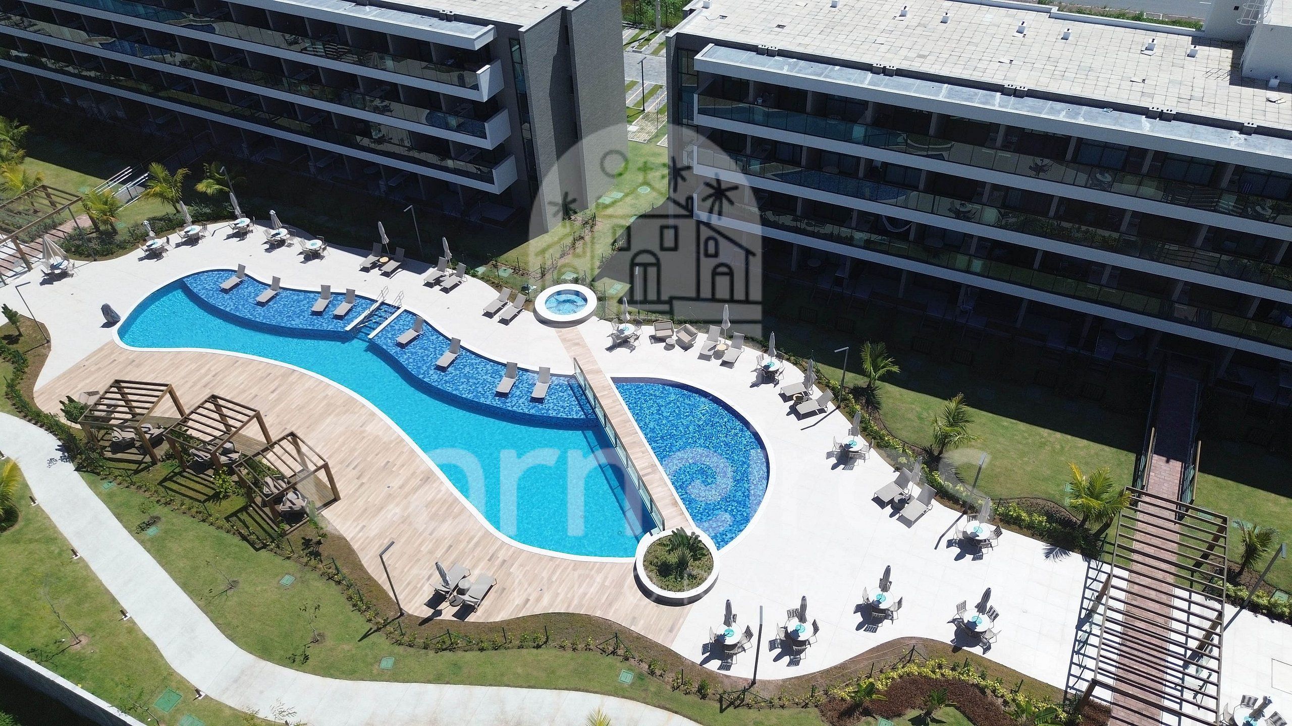 An aerial view of a resort with a large swimming pool, sun loungers, and a small circular hot tub.