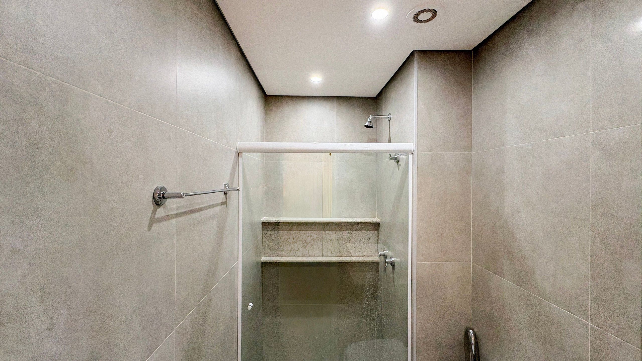 A modern bathroom with a glass shower enclosure, a towel rack, and a visible showerhead.