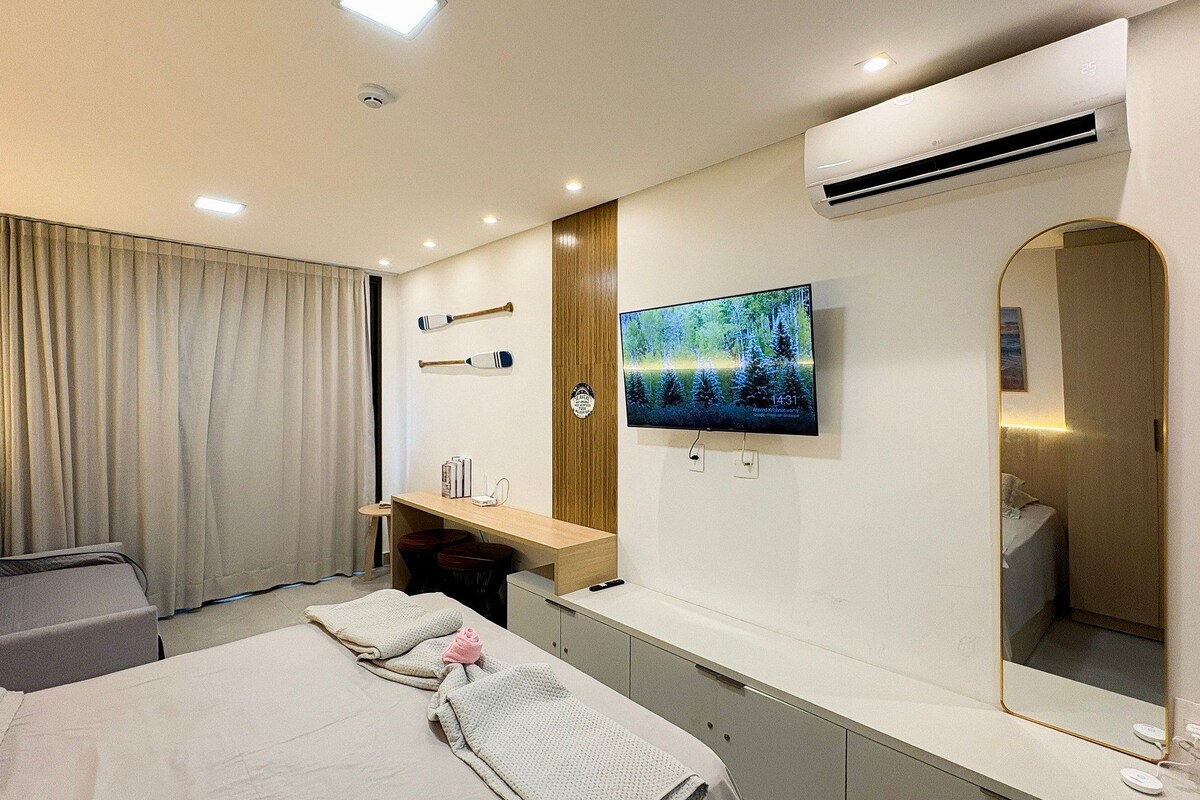 Quarto de hotel com cama, televisão, escrivaninha e espelho.