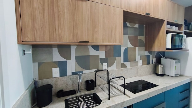 Una cocina con armarios de madera, microondas, hervidor y pileta.