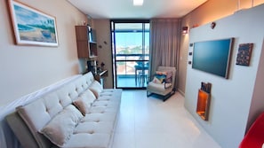 A modern living room with a sofa, a chair, a TV, and a balcony with a view. - Beach Class Summer Residence  (Ipojuca)