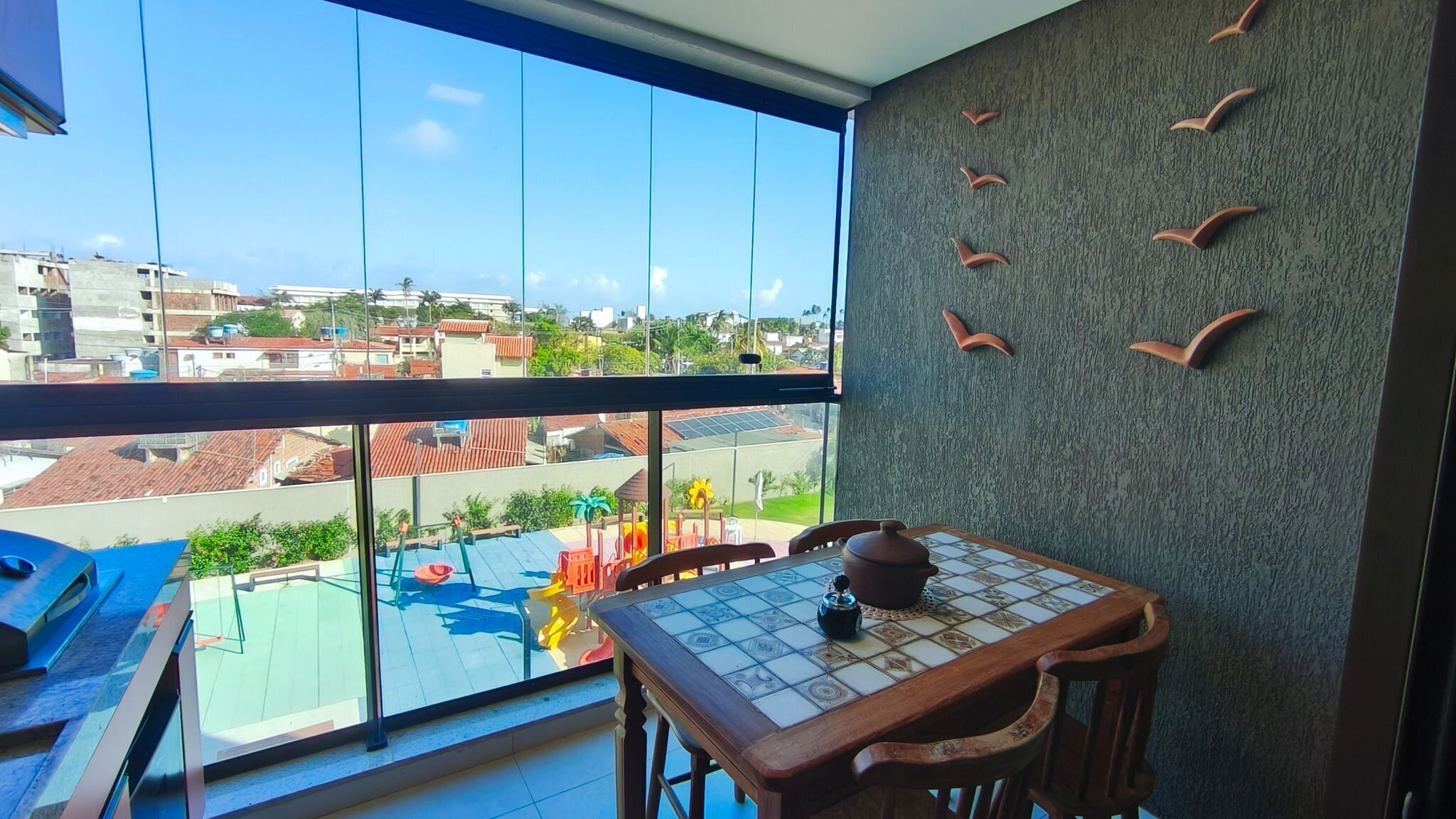 A balcony with a view of a residential area, a tiled table with a teapot, and a wall with bird-shaped decorations.