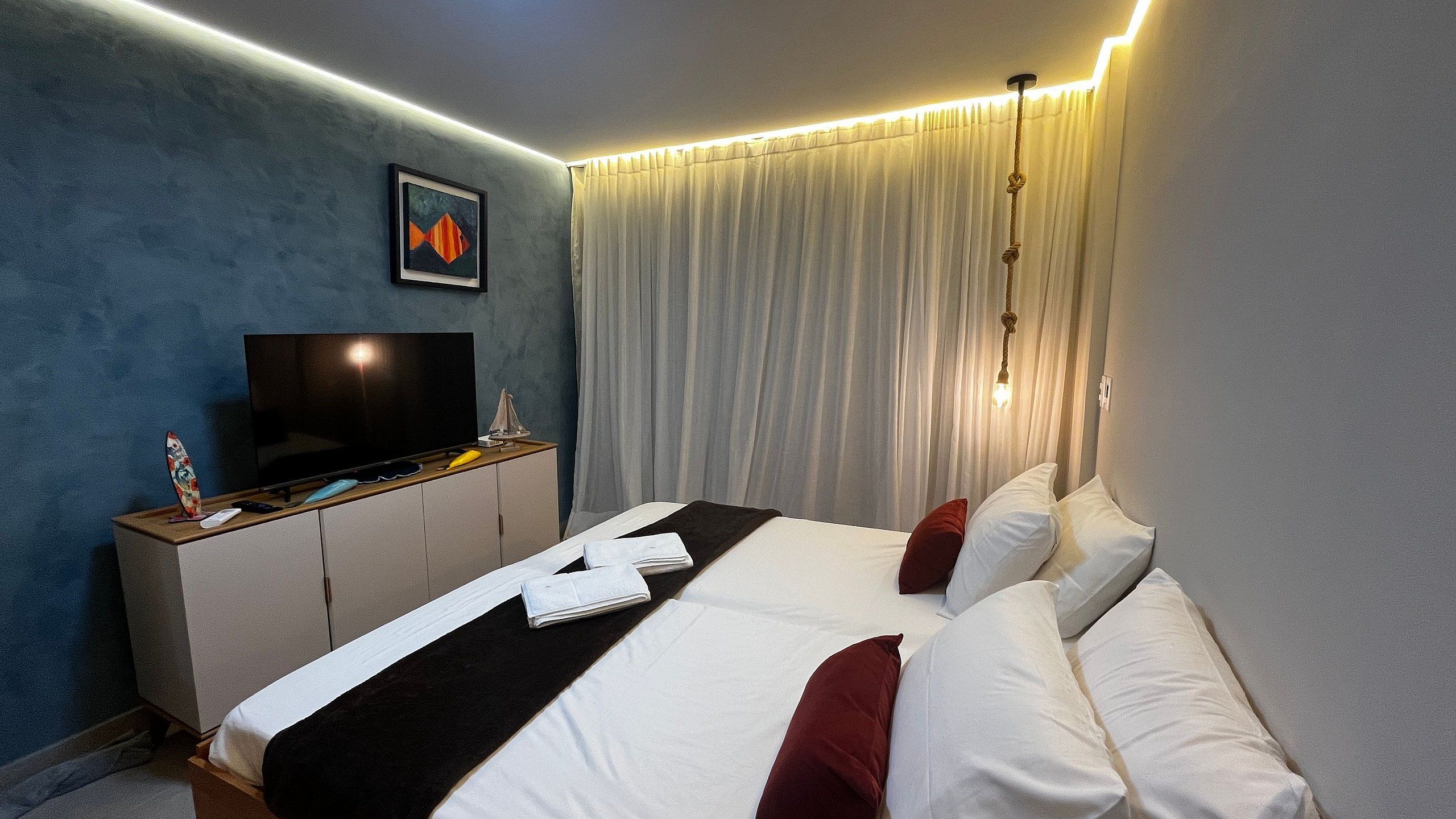 A hotel room with a bed, a television, a minibar, and a curtain.
