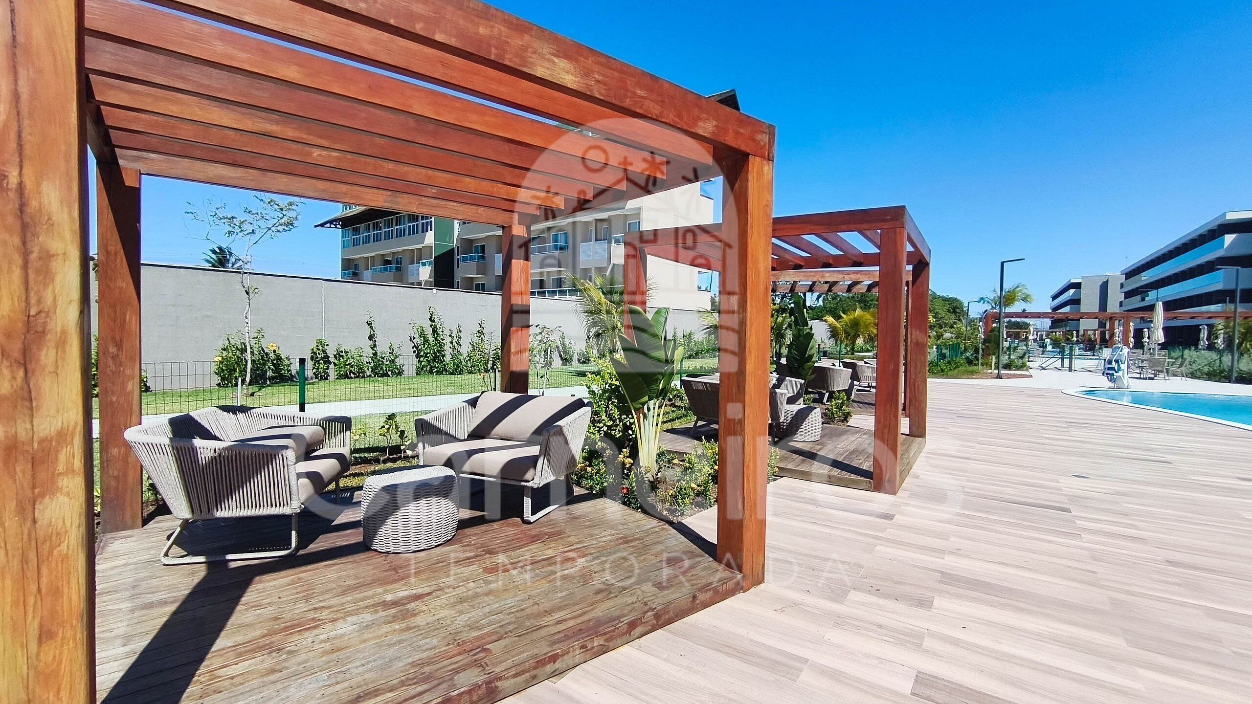 A wooden deck with outdoor furniture, a pool, and a view of modern buildings.