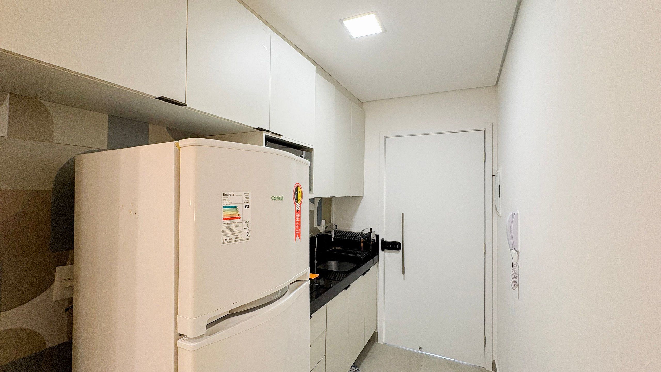 A compact kitchen with a white refrigerator, a black countertop, and a white door.