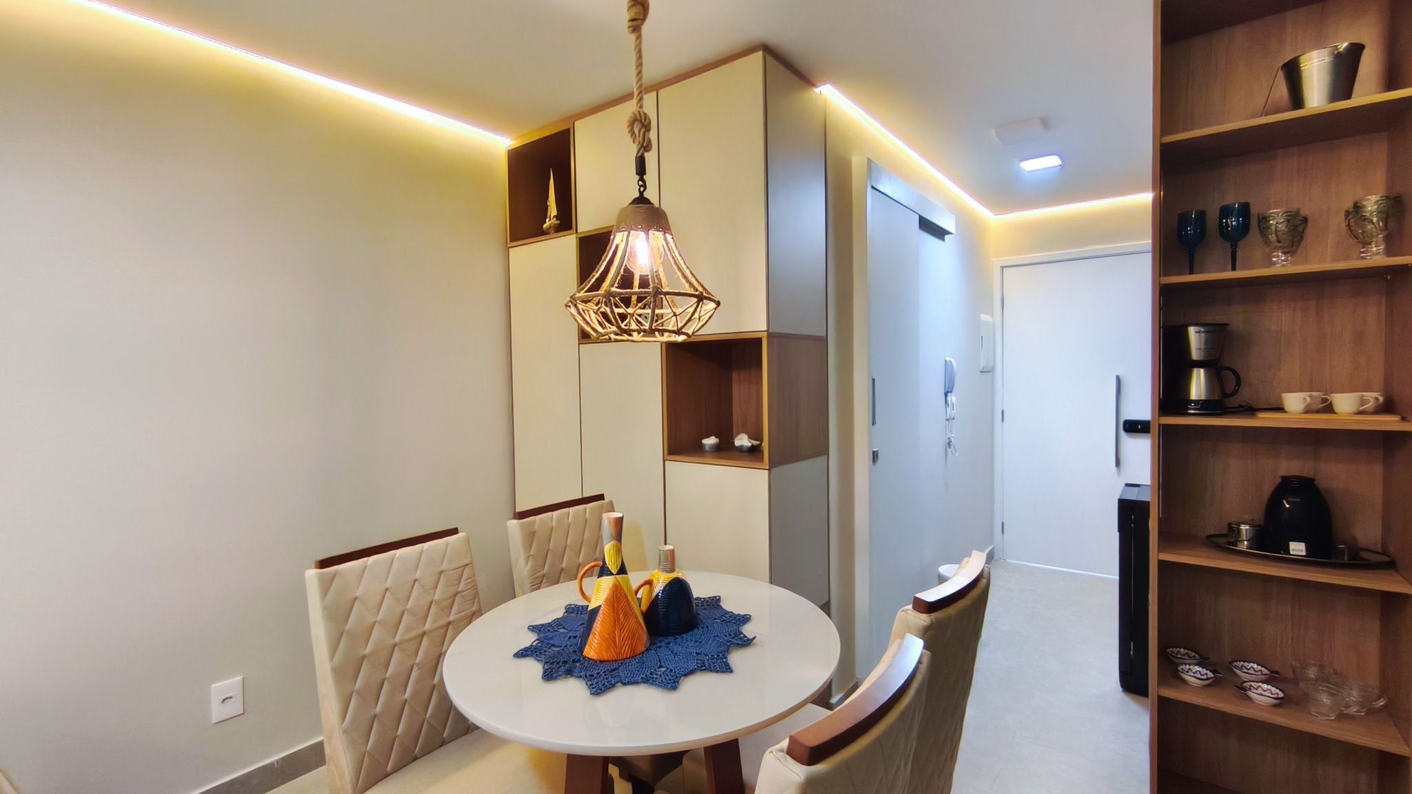 Uma área de refeições moderna com uma mesa redonda, cadeiras, um objeto decorativo central e um lustre.