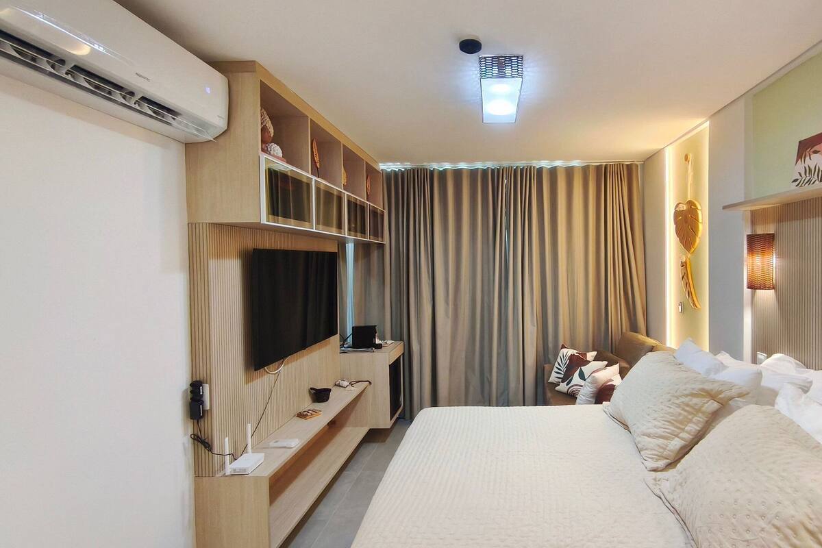 Une chambre d’hôtel avec un lit, une télévision, une étagère avec quelques objets et un rideau.