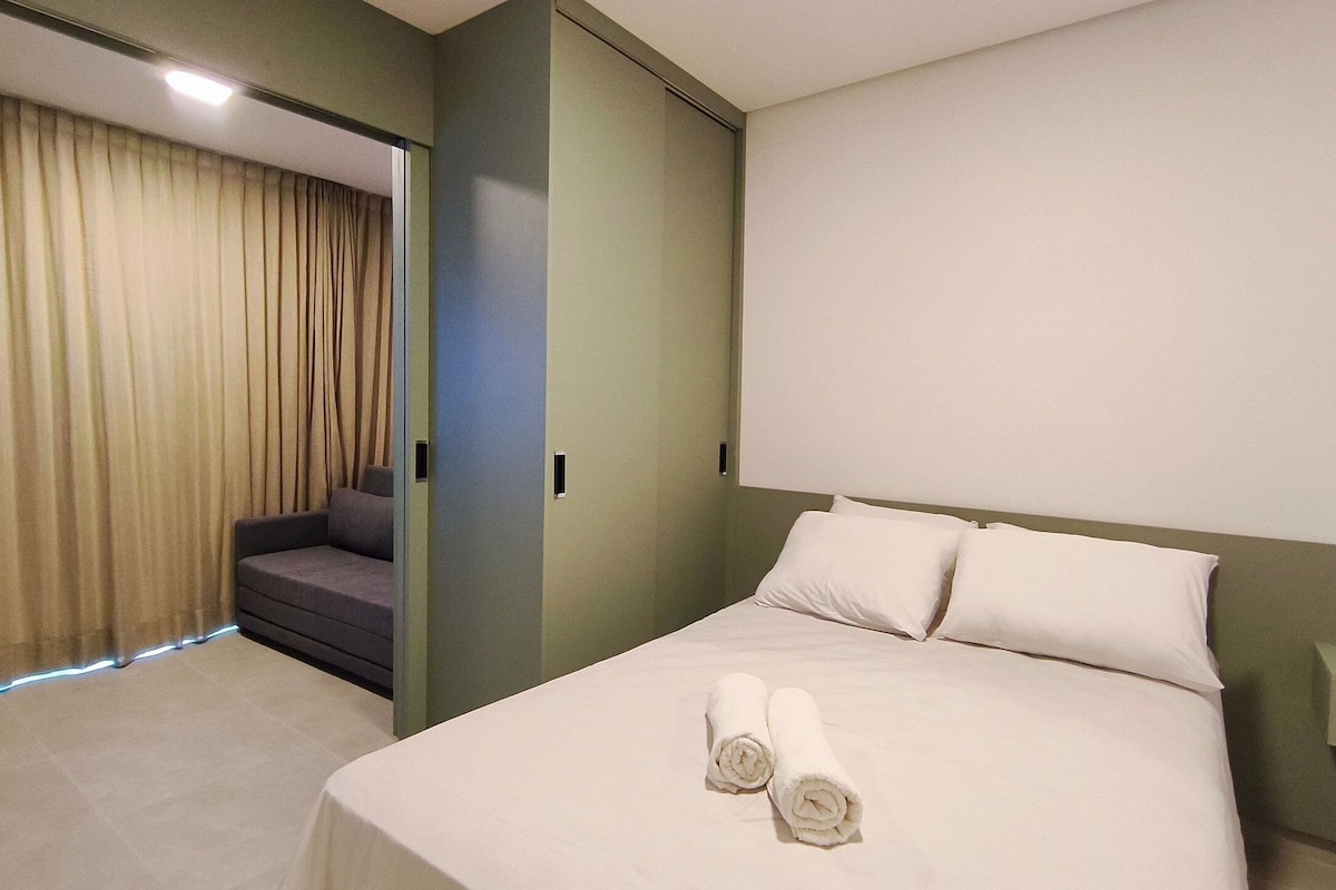 A hotel room with a bed, two pillows, a nightstand, a chair, and a curtain.