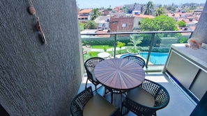 A balcony with a table and chairs, a pool, and a view of a residential area.