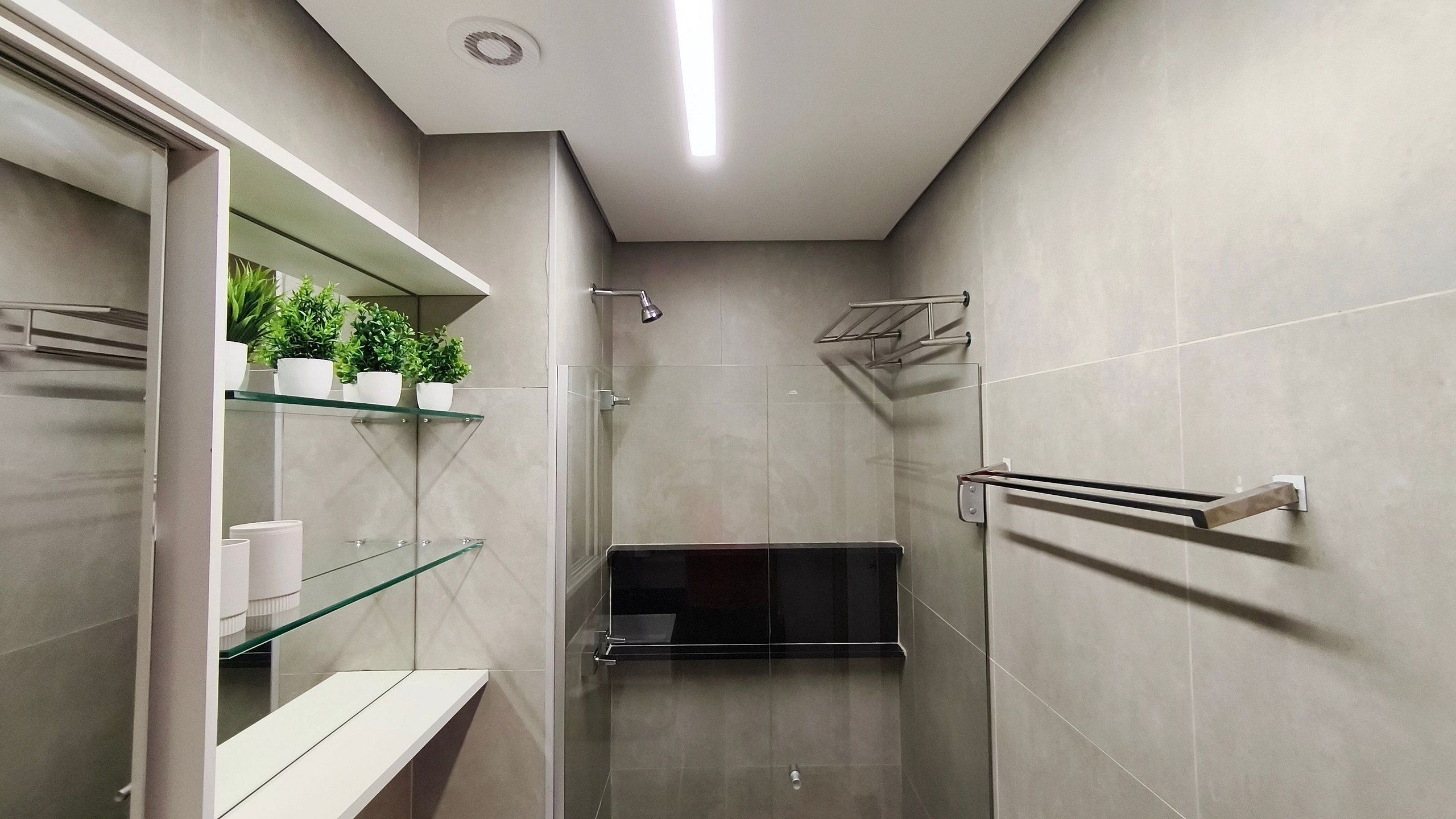 Een moderne badkamer met een douchecabine van glas, een inbouwkastje met toiletartikelen en een handdoekrek.