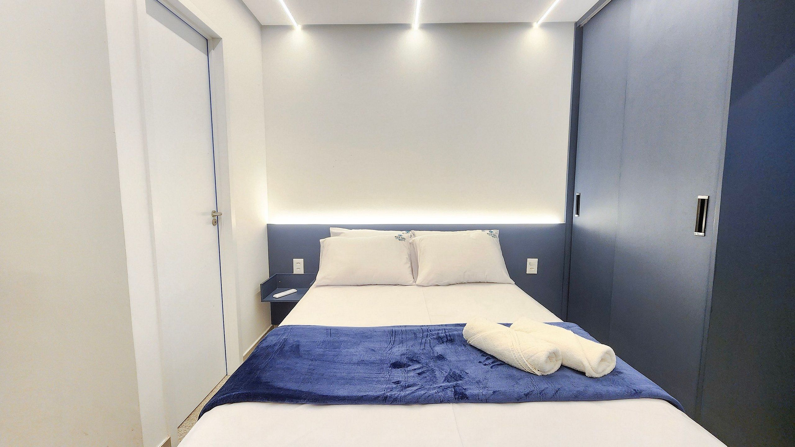 Quarto de hotel com cama, mesas de cabeceira e uma porta, parede azul.