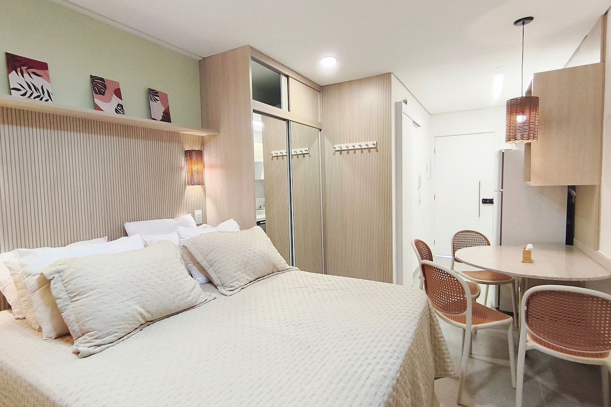 A bedroom with a bed, bedside tables, a mirror, a small round table with chairs, and a hanging light fixture.