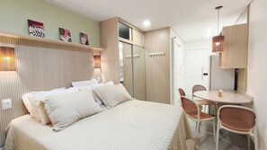 A bedroom with a bed, bedside tables, a mirror, a small round table with chairs, and a hanging light fixture. - Beach Class Summer Residence  (Ipojuca)