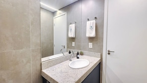 Une salle de bain moderne avec un grand miroir, un lavabo blanc et deux serviettes accrochées au mur.