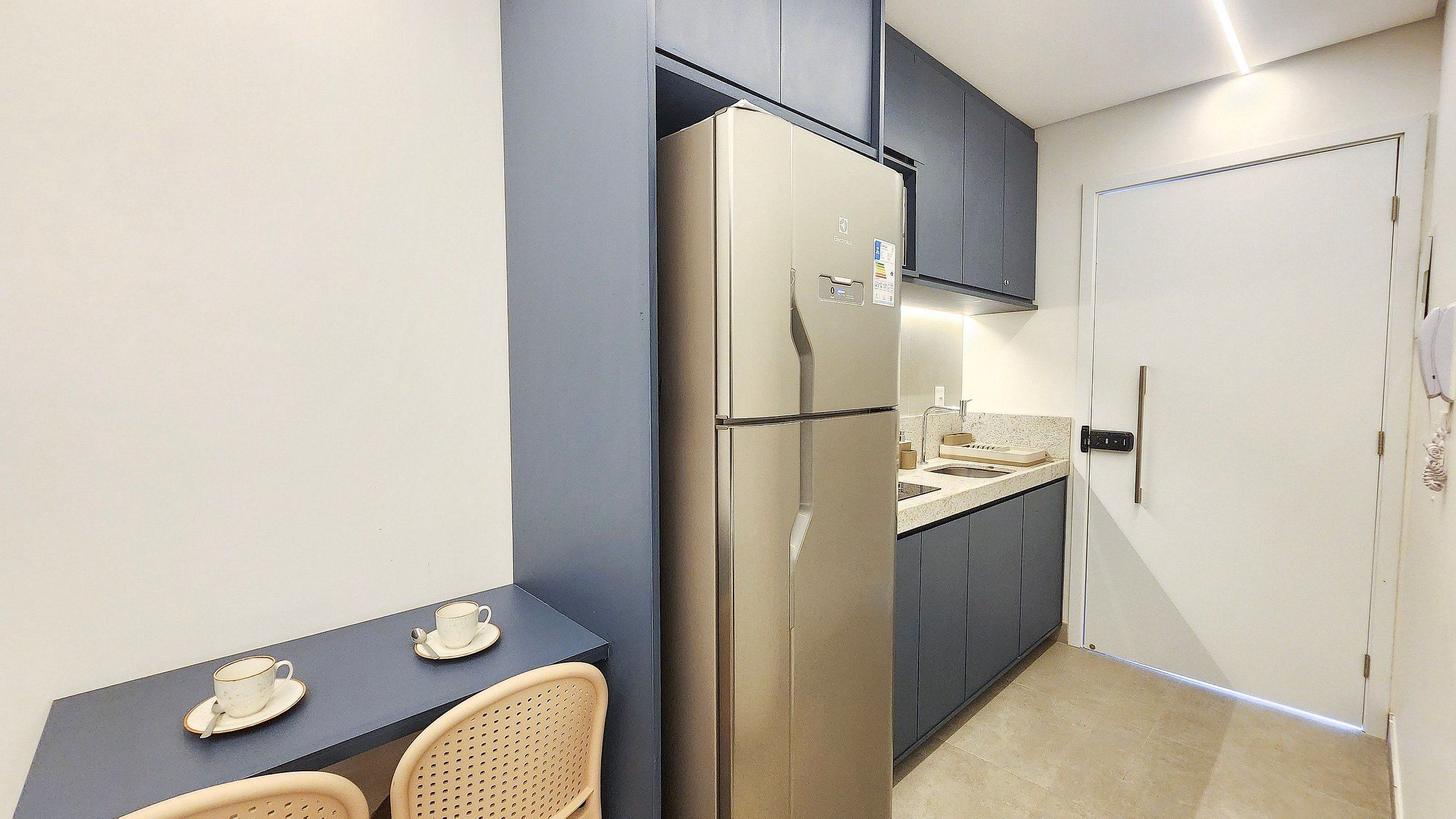 A compact kitchen with a refrigerator, a sink, and a small dining area with chairs and a table.