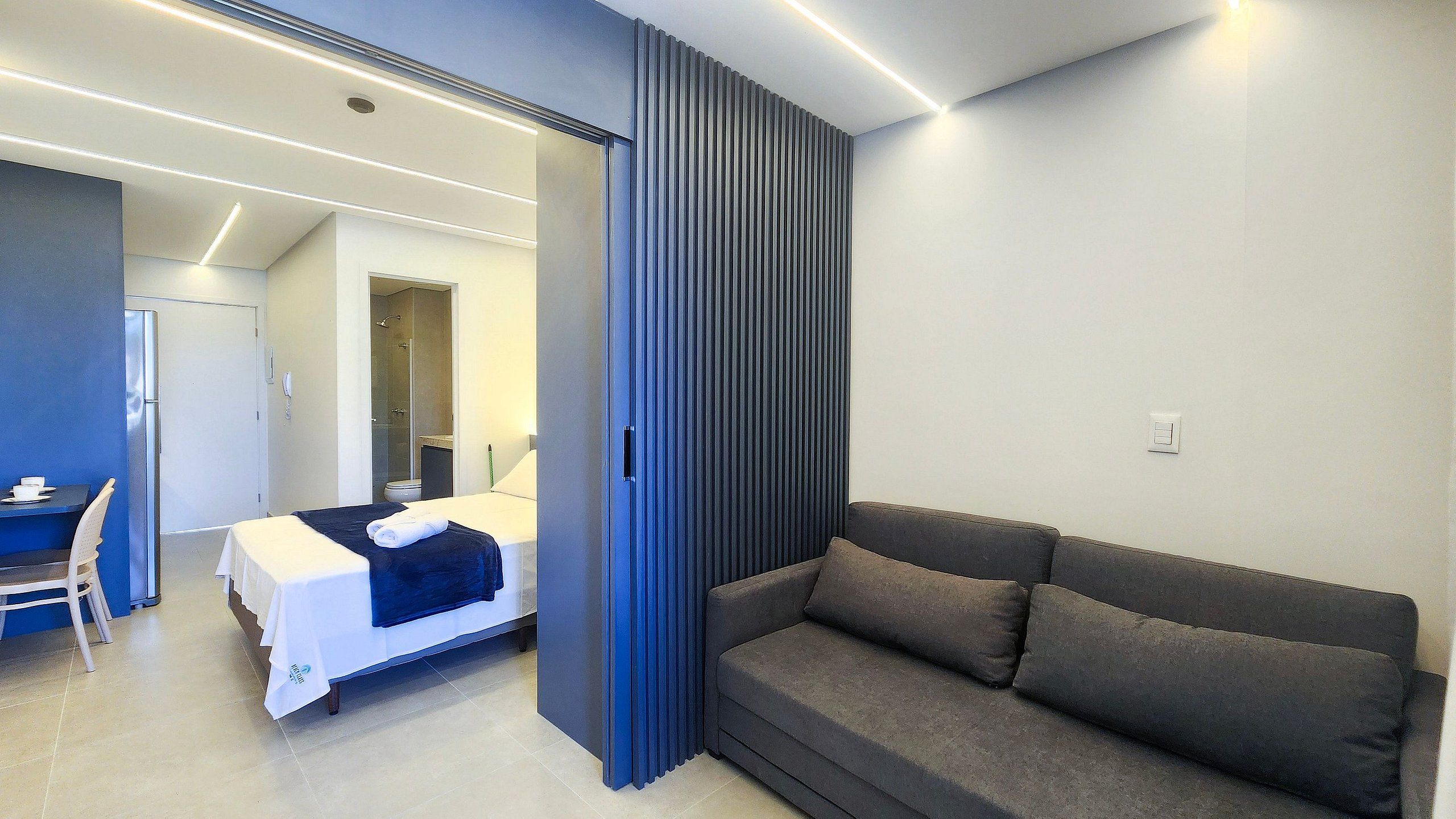Habitación de hotel moderna con cama, sofá, escritorio y baño visible a través de una puerta abierta.