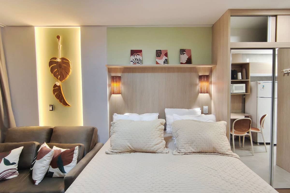 Una habitación de hotel con una cama, dos mesitas de noche, un escritorio, una silla, un armario y decoración en la pared.