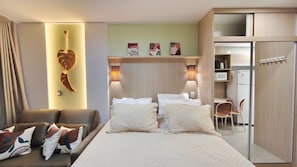 A hotel room with a bed, two bedside tables, a desk, a chair, a wardrobe, and wall art.