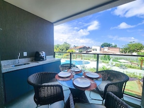 Un balcon doté d’un coin cuisine, d’une table à manger avec des chaises, et offrant une vue sur une piscine et des bâtiments.