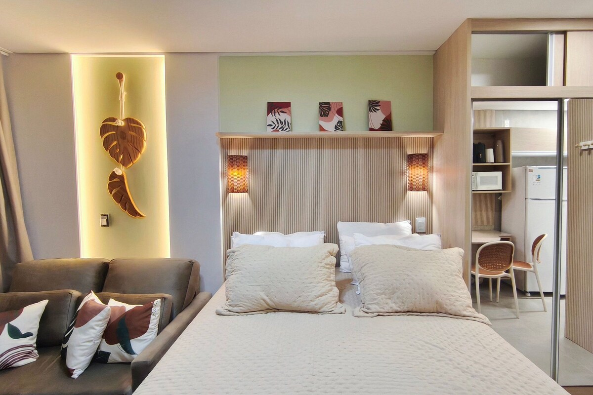 Quarto de hotel com cama, duas mesas de cabeceira, escrivaninha, cadeira, guarda-roupa e obras de arte na parede.