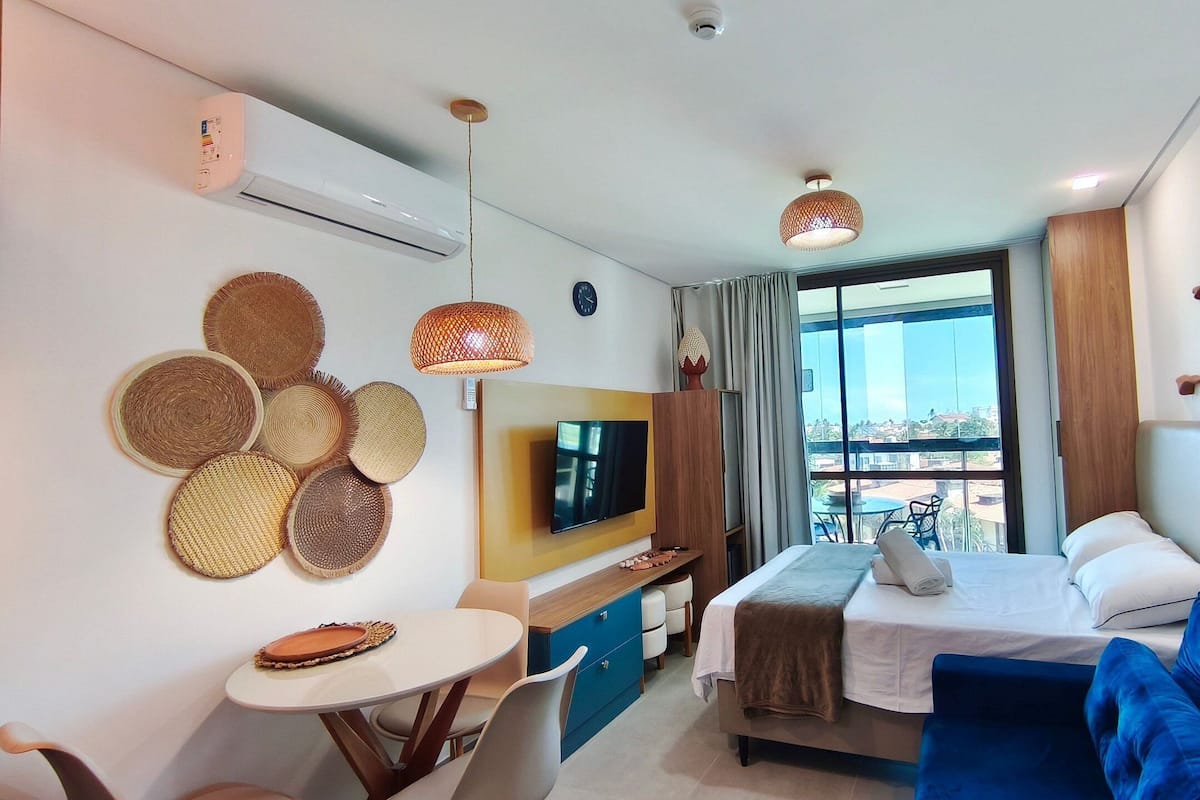 A hotel room with a bed, a TV, a dining table, and a view of the city.