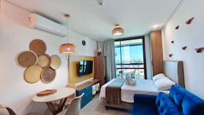 A hotel room with a bed, a TV, a dining table, and a view of the city. - Beach Class Summer Residence (Ipojuca)