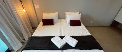 A hotel room with a bed, pillows, a blanket, and a towel.