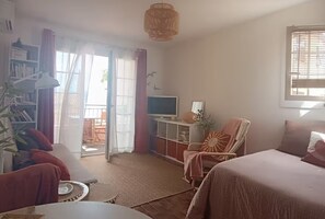 A room with a sofa, a chair, a TV, and a bookshelf. - Studio 🔆 just a few meters from the beach.  Ideal for couples or solo. (Agay)