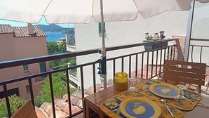 A balcony with a table set for two, an umbrella, and a view of the sea.