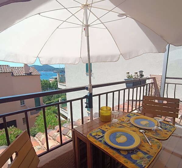 A balcony with a table set for two, an umbrella, and a view of the sea. - Studio 🔆 just a few meters from the beach.  Ideal for couples or solo. (Agay)