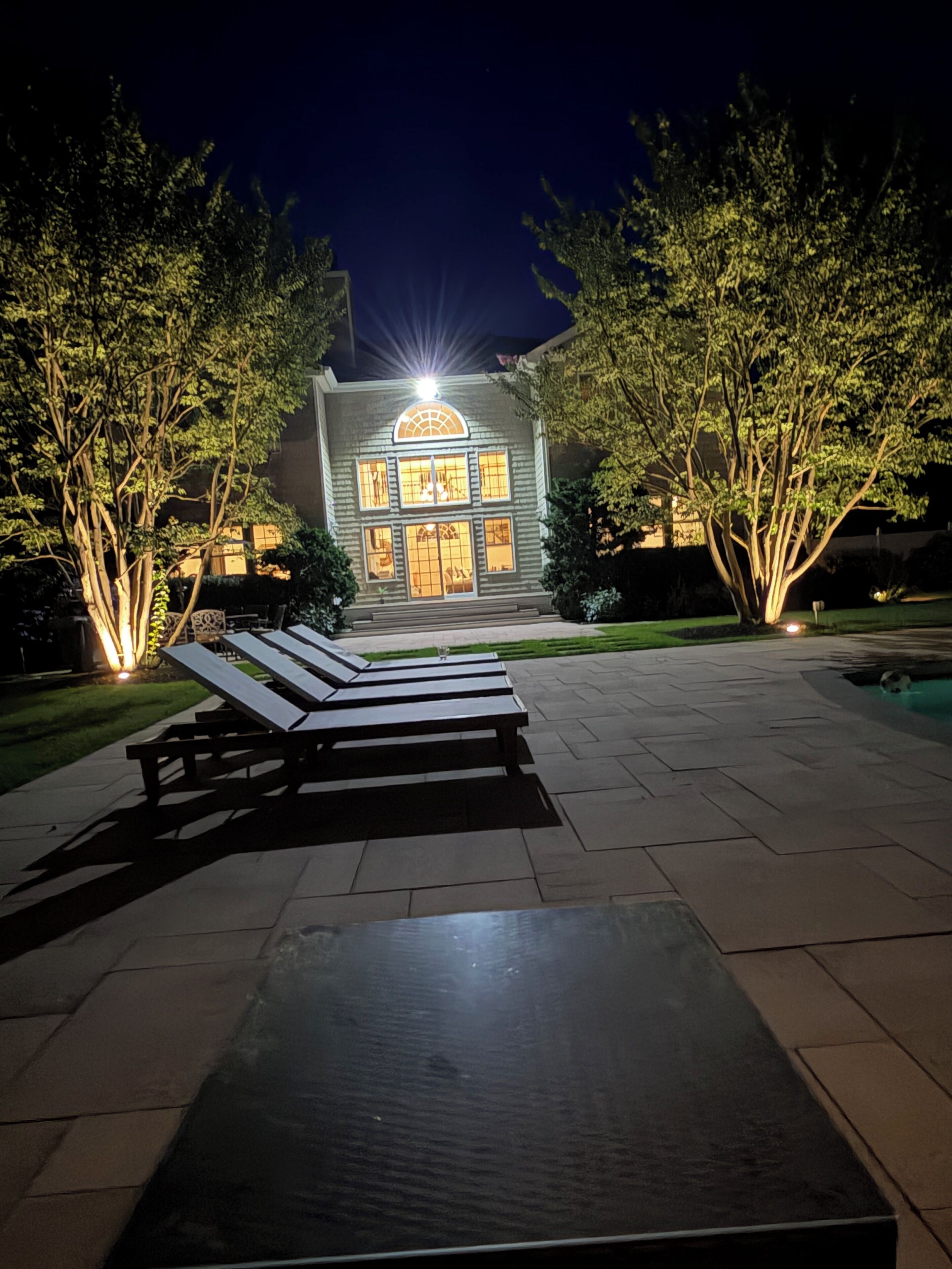 Una casa con entrada iluminada, asientos exteriores y piscina.