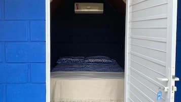 A small, enclosed room with a bed, a window, and a door.
