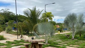 A garden with stone tables and chairs, surrounded by grass and palm trees. - Pousada Ramilos - Sertão (Tiangua)